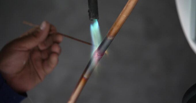 A technician or worker is soldering copper pipes; an air conditioning technician.