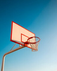 Bright orange basketball hoop and white backboard against deep clear blue sky