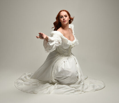 full length portrait beautiful female model wearing historical white fantasy wedding dress, fairytale ball gown. isolated figure sitting pose, hands gesturing  on white studio