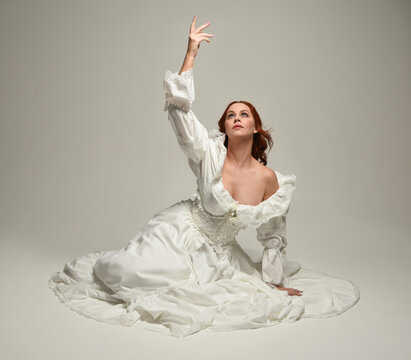 full length portrait beautiful female model wearing historical white fantasy wedding dress, fairytale ball gown. isolated figure sitting pose, hands gesturing  on white studio
