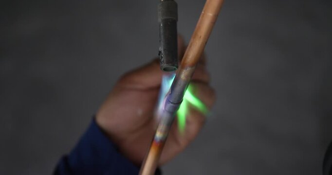 A technician or worker is soldering copper pipes; an air conditioning technician.