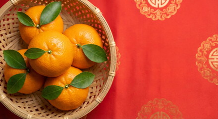 A picture of vibrant mandarin oranges in a bamboo basket against a bright red background adorned with gold patterns&mdash;a symbol of good fortune, wealth, and prosperity for the Chinese New Year celebratio