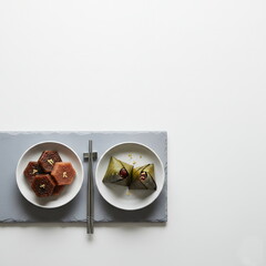 Generated AI | Elegant Minimalist Top-Down View of Traditional Asian Rice Dumplings and Hexagonal Honey Cakes Decorated with Edible Gold Leaves on a Sleek Slate Platter.
