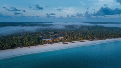 Fototapeta premium Showing beachfront villas strip stretching along white sand beach at dawn, with palm trees, mist
