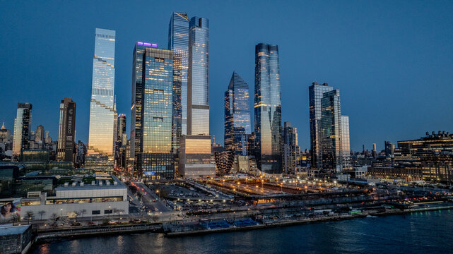 Aerial view of gleaming skyscrapers pierce the twilight sky over the Hudson Yards, their lights reflecting on the water, New York, New York, United States.