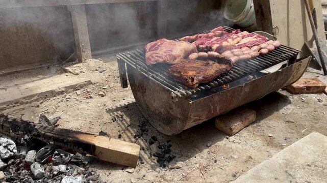 Authentic Argentine asado featuring traditional meat cuts: tira de asado (short ribs), chorizo sausage, and vacio (flank steak) cooking on an improvised grill at a construction site