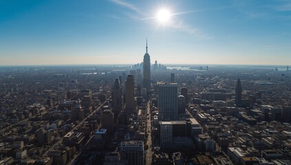 Obraz premium Rising tall skyscraper spire above downtown skyline showing rooftops, shadowed avenues and harbor