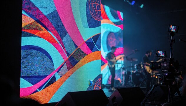 LED wall displaying dynamic visuals in focus during a hybrid concert with the performer and stage equipment out of focus in the background.