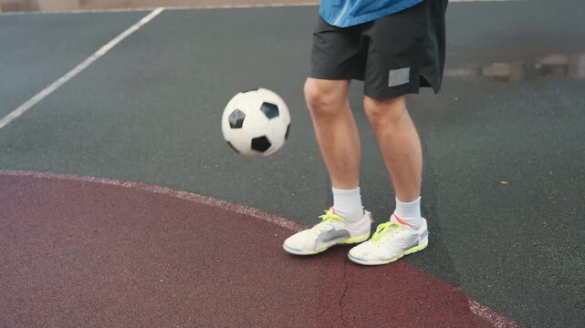 Rainy court soccer player juggling ball, wet asphalt and puddles, blue jacket and black shorts, neon sneakers, closeup of legs and ball control, rhythmic touches with light splashes, street training