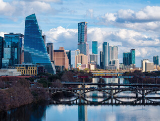 Fototapeta premium Clouds hover over the Austin skyline as buildings reflect on the calm waters of the Colorado river during late afternoon.
