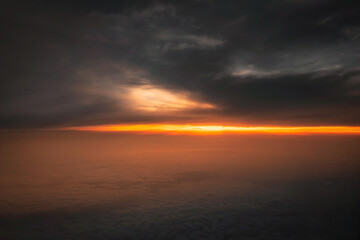 Fototapeta premium Aerial view of dramatic sunset over the sea of clouds. Orange sunlight breaking through dark storm clouds creating a moody atmosphere.