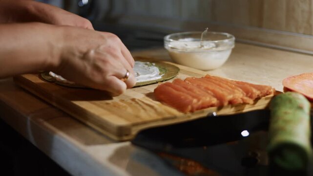 Hand laying salmon slices as filling on a green spinach pancake anointed with creamy cheese