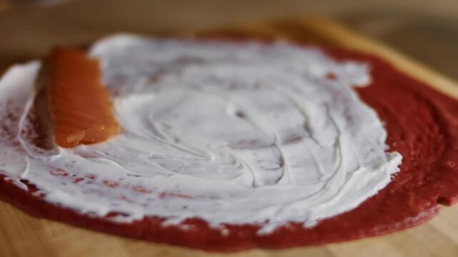 Adding salmon slices as filling on red pancake anointed with creamy cheese, close up