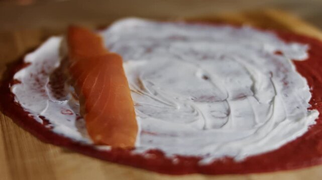 Laying salmon slices as filling on a red pancake anointed with creamy cheese, close up
