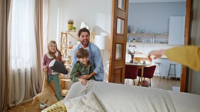 Parents playing children home running around cozy sofa. Happy family having fun