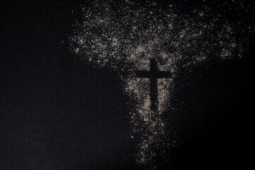 A cross shape formed in scattered ashes on a dark textured background represents the symbolic meaning of Ash Wednesday and repentance.