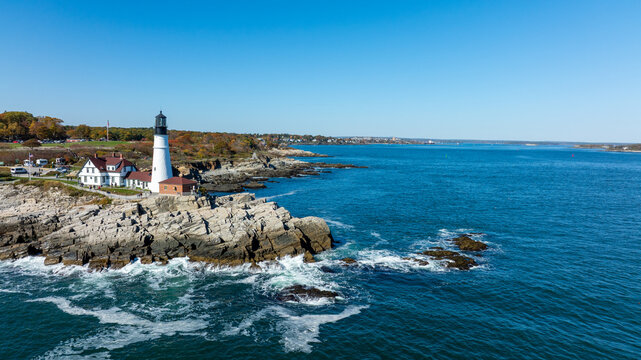 Aerial view of the iconic Portland Head Light standing tall against the rugged coastline, where the sapphire sea meets the rocky shore, Cape Elizabeth, Maine, United States.