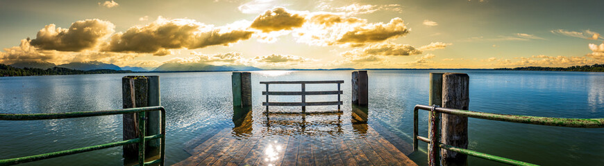 wooden pier with mountains in the distance, reflecting on calm water in the early morning light
