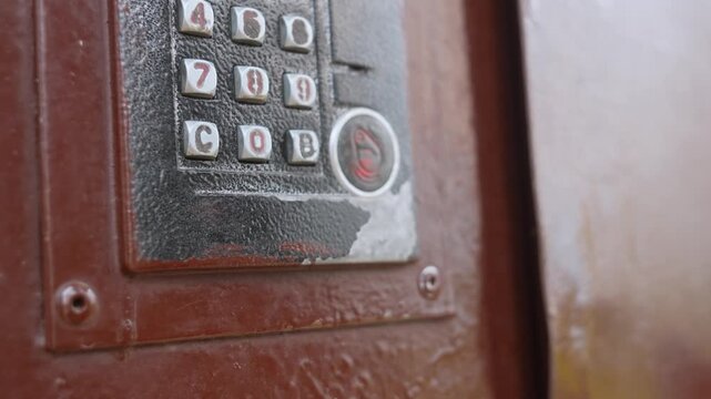 Woman's hand holding a blue electronic key fob and a bunch of keys, opening the front door by placing the contactless access key on the reader of the intercom system to unlock it