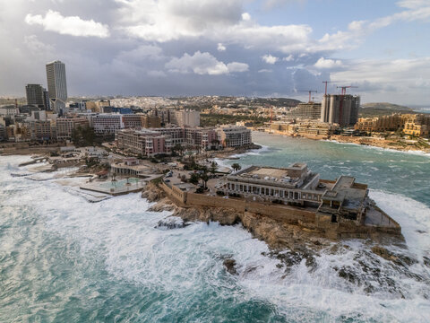 Aerial view of the Corinthia Hotel and the surrounding buildings, as the choppy azure sea crashes against the rocky coastline, St. Julian's, St. Julian's, Malta.