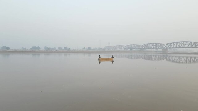 An aerial shot of a boat in the river with fishermen inside, a long and huge bridge can be seen in the background. 4K drone shot. 