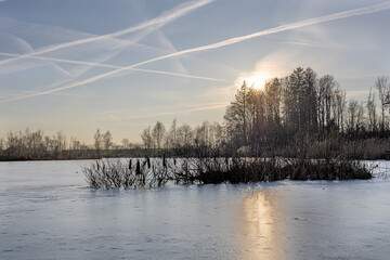 Winter sunset over frozen lake with forest and soft sun reflection. Serene winter landscape featuring a frozen lake with smooth ice, soft sunset light reflecting on the surface and bare forest trees 