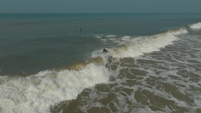Aerial view of a surfer riding the crest of a wave, with the sea stretching to the horizon, Kodi Bengare, Karnataka, India.