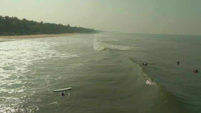 Aerial view of surfers catching waves in the ocean with a surfboard on the beachside at Kodi Bengare, showcasing the vibrant coastal life, Kodi Bengare, Karnataka, India.