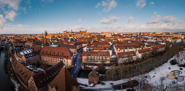 Aerial view of the medieval city's red rooftops and snow-dusted parks stretch under a blue sky, framed by the Pegnitz River, Nurnberg, Germany.