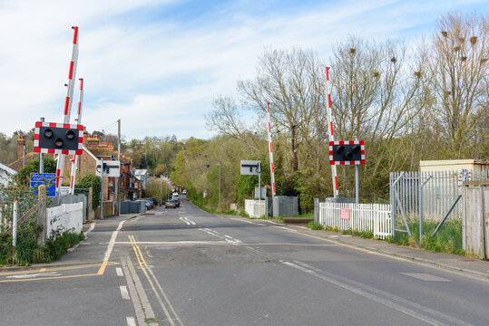Level crossing with signals along a road running through a small town in the countryside of England on a partly cloudy spring day