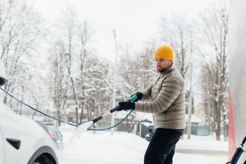 Man washing electric car in a winter self-service car wash