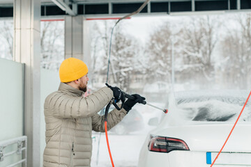 Man washing electric car at self-service station in winter
