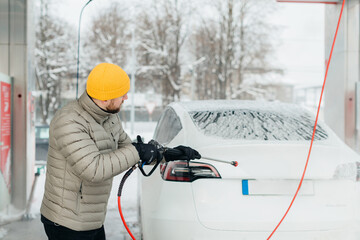 Obraz premium Man washing electric car at self-service car wash in winter