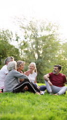 Naklejka premium Group of diverse senior friends relaxing, talking, and laughing while sitting on the grass outdoors, enjoying togetherness in nature