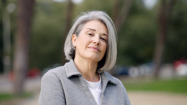 Confident mature woman with grey hair smiling, enjoying an outdoor moment. Expressing elegance and positive aging