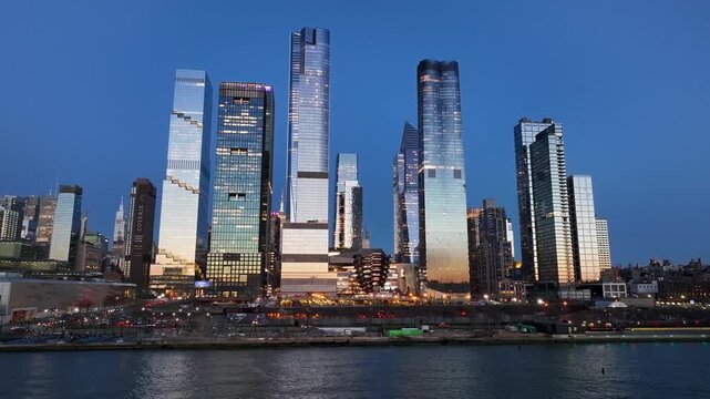 Aerial view of Hudson Yards' skyscrapers reflecting twilight, creating a dazzling display of light and form against the dark blue sky, New York, New York, United States.