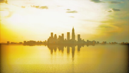 Obraz premium A vibrant sunset paints the sky in shades of orange and gold, casting a beautiful glow over the city skyline. The calm water reflects the silhouette of buildings, creating a peaceful scene.