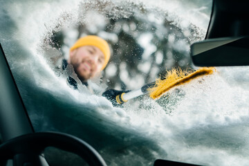 Person clearing snow from electric car windshield in winter