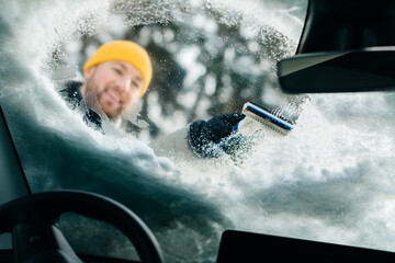 Man scraping snow and ice from car windshield
