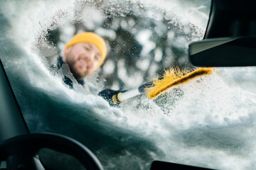 Man clearing snow and ice from car windshield in winter