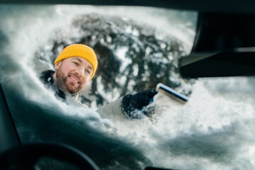 Man smiling scraping snow from car windshield in winter