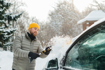 Man clearing snow from electric car windshield in winter