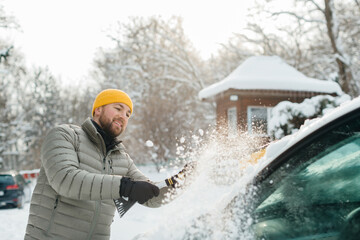 Man clearing snow from car windshield in winter