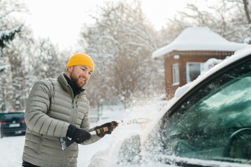 Man clearing snow from car windshield in winter