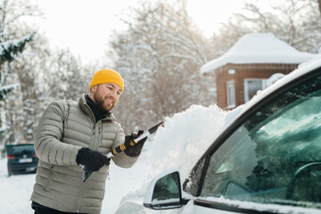 Man clearing snow from electric car windshield in winter