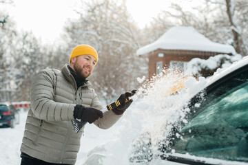 Man clearing snow from car windshield in winter