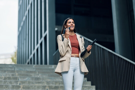 Pretty young business woman using her smartphone while going down street stairs