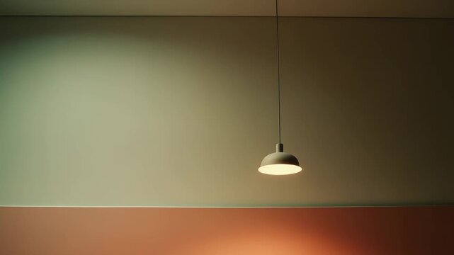 Suspended ceiling lamp casting a warm glow onto a two tone wall, featuring a subtle green upper portion and a vibrant orange lower section, creating a modern minimalist interior design element