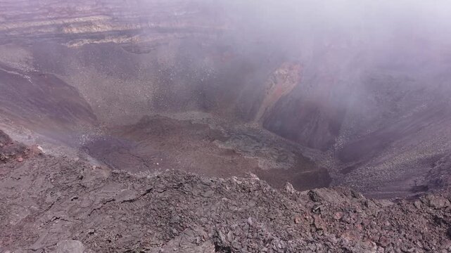 Drone footage flying toward the edge of a volcanic crater at Piton de la Fournaise on Reunion Island, with the camera gradually tilting down while continuing forward.