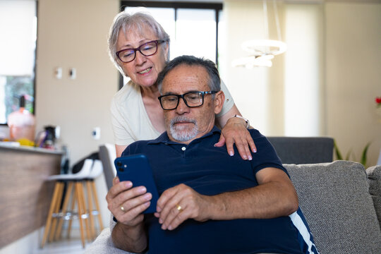 A couple of grandparents checking social media and technology on the sofa at home, sharing news they have found.